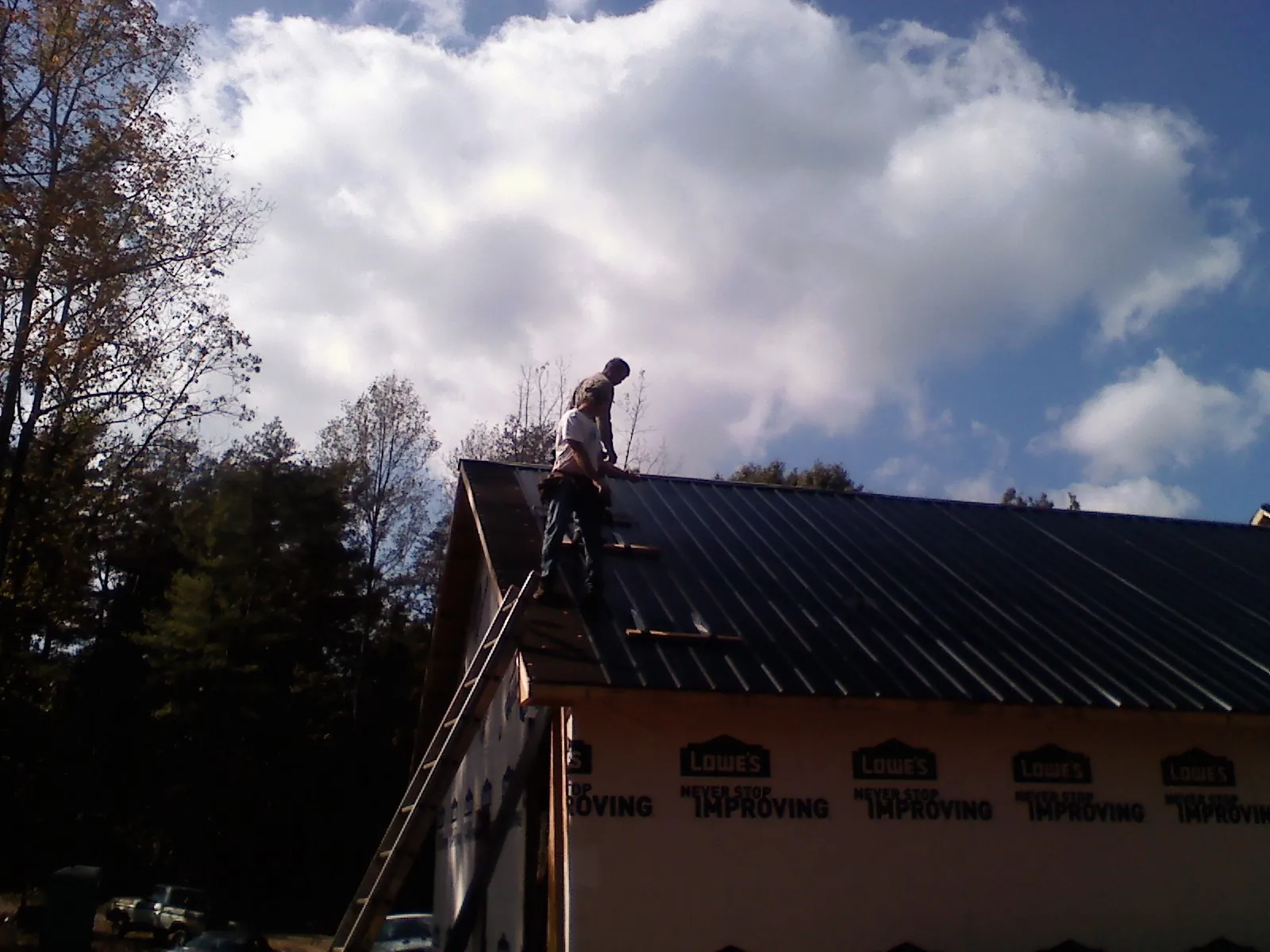 Roofer fastening dark metal panels high against a cloudy sky, from a Roof Inspection job in Holbrook